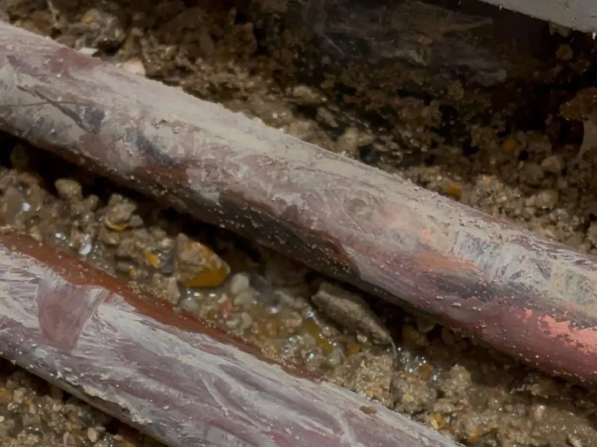 Exposed copper heating pipes lie in wet material beneath the bathroom floor