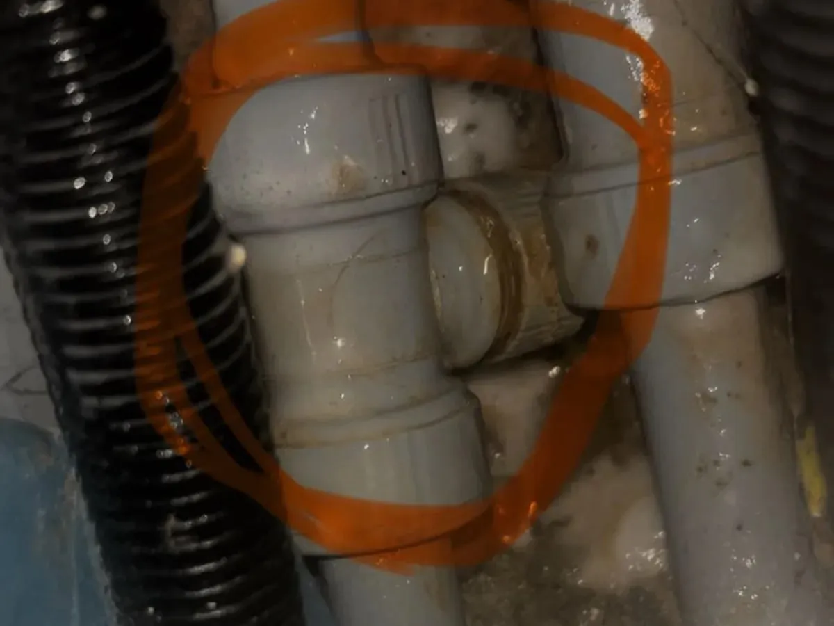 Close-up of the white pipe fitting inside the opened boxing, with the fault circled in orange in the published photograph