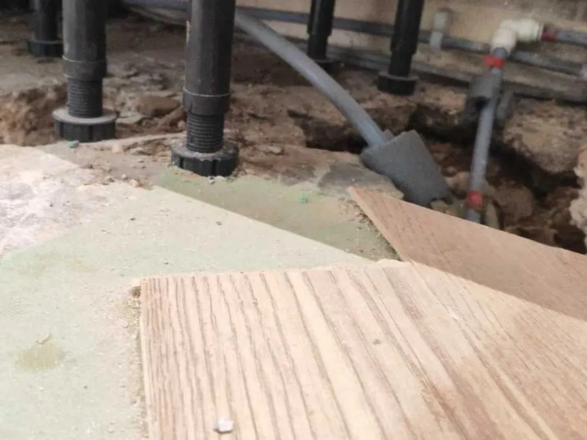 Replacement flexible pipework runs through the opened floor beneath the kitchen units