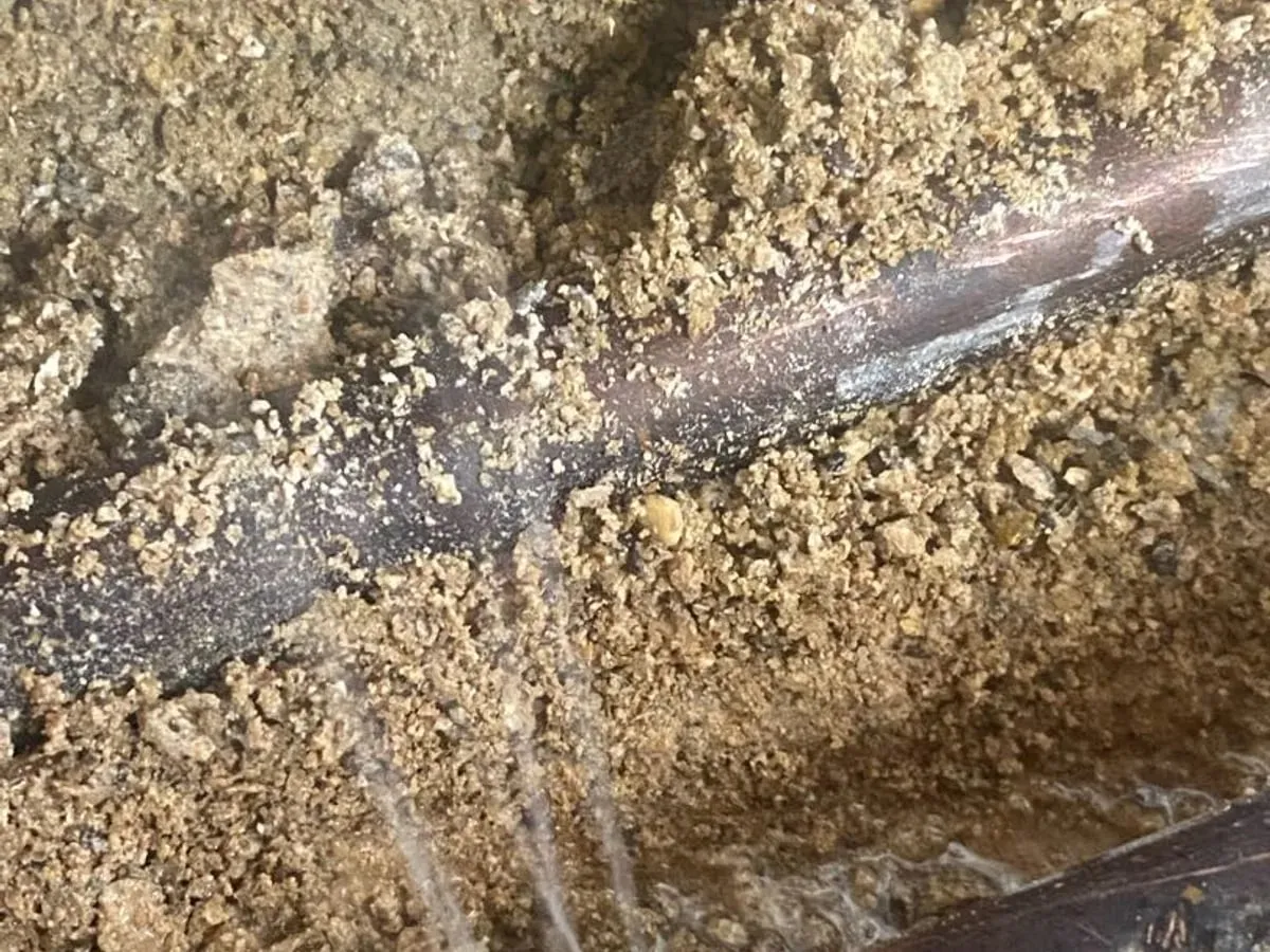 Water spraying from an exposed copper pipe into the surrounding floor material