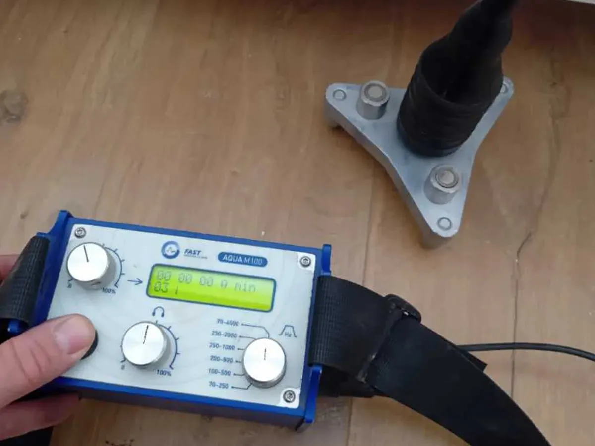 A FAST AQUA M100 amplifier connected to a microphone on a three-legged contact foot on a plywood subfloor